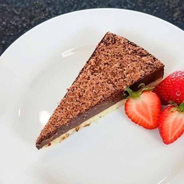 Slice of chocolate tart topped with grated chocolate, served on a white plate with two fresh strawberries
