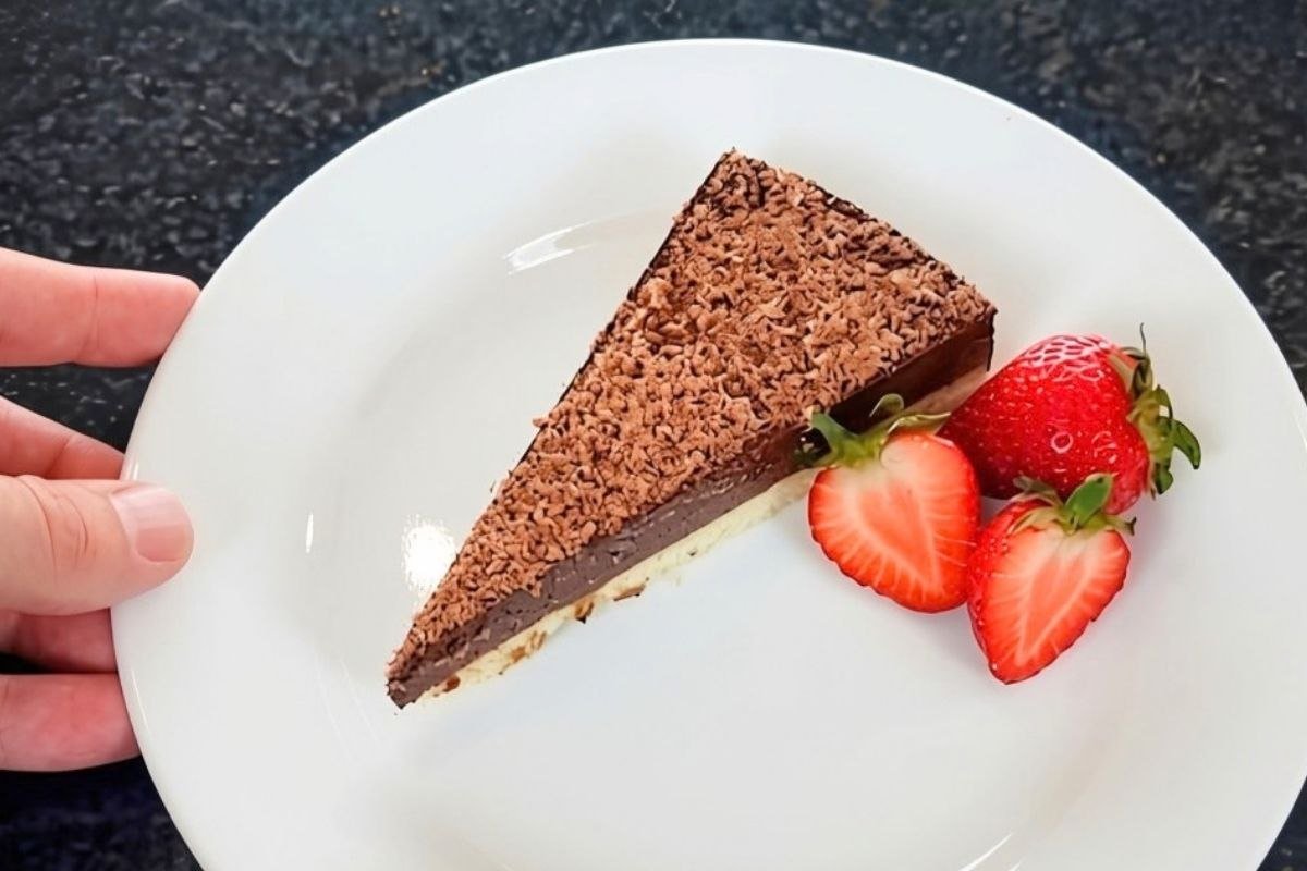 Slice of chocolate tart topped with grated chocolate, served on a white plate with two fresh strawberries