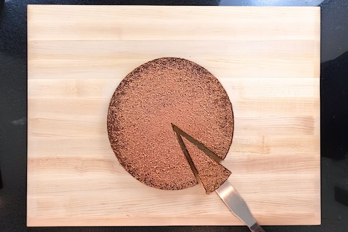Overhead view of a cocoa dusted chocolate tart on a wooden board with a slice being lifted out