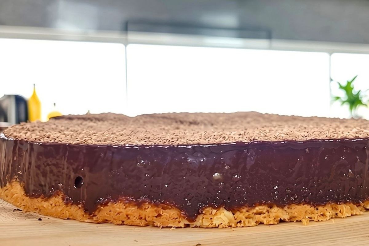 Side view of a chocolate tart with a glossy ganache top, grated chocolate and a biscuit crumb base