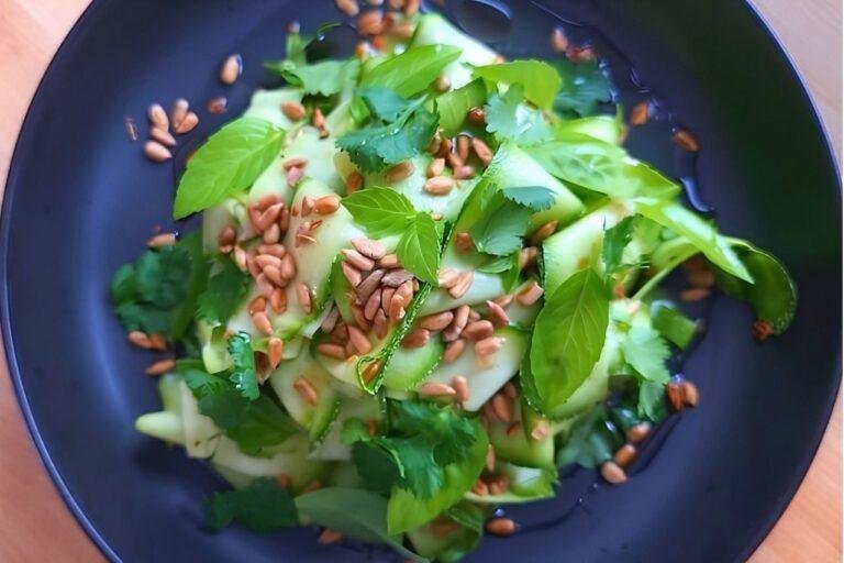 Fresh courgette zucchini salad topped with sunflower seeds and vibrant herbs, served in a dark bowl.