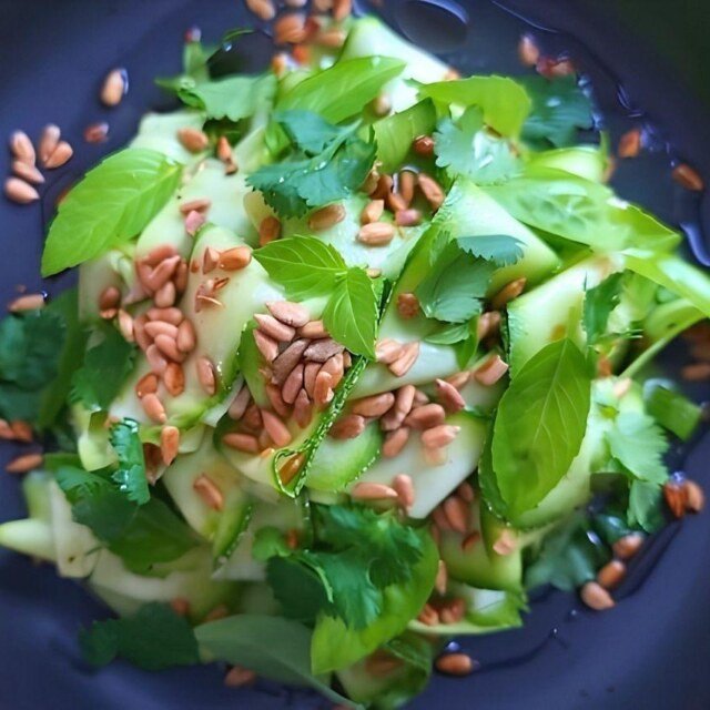 Fresh courgette zucchini salad topped with sunflower seeds and vibrant herbs, served in a dark bowl.