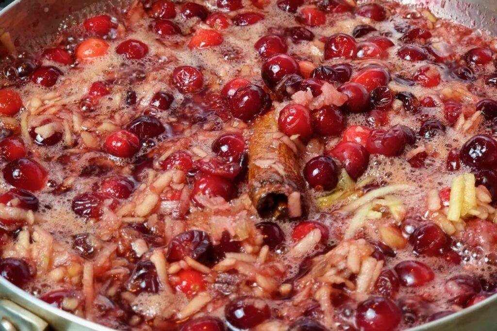 Close up of bubbling cranberry sauce with a cinnamon stick and grated ginger