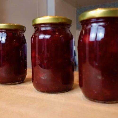 Three jars of dark red cranberry sauce with gold lids on a wooden counter