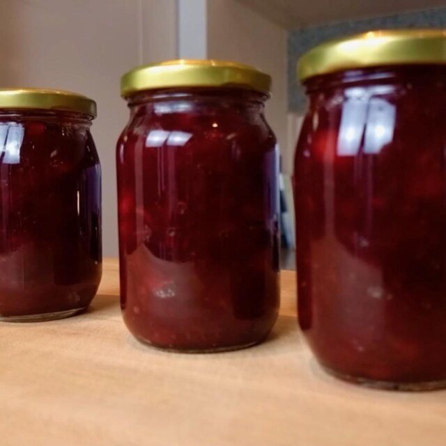 Three jars of dark red cranberry sauce with gold lids on a wooden counter