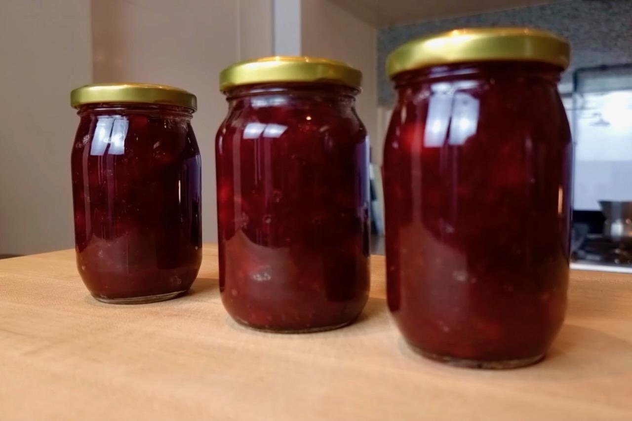 Three jars of dark red cranberry sauce with gold lids on a wooden counter