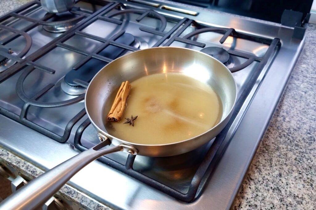 Steel pan of syrup with a cinnamon stick and star anise on a gas hob