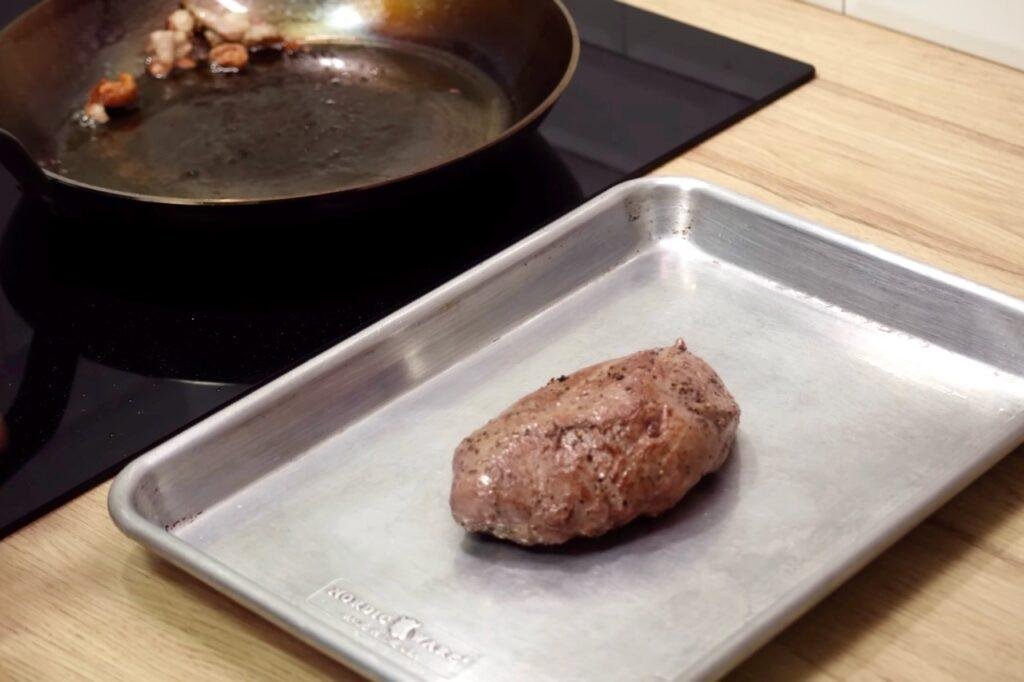 Seared duck breast on a metal tray beside a frying pan