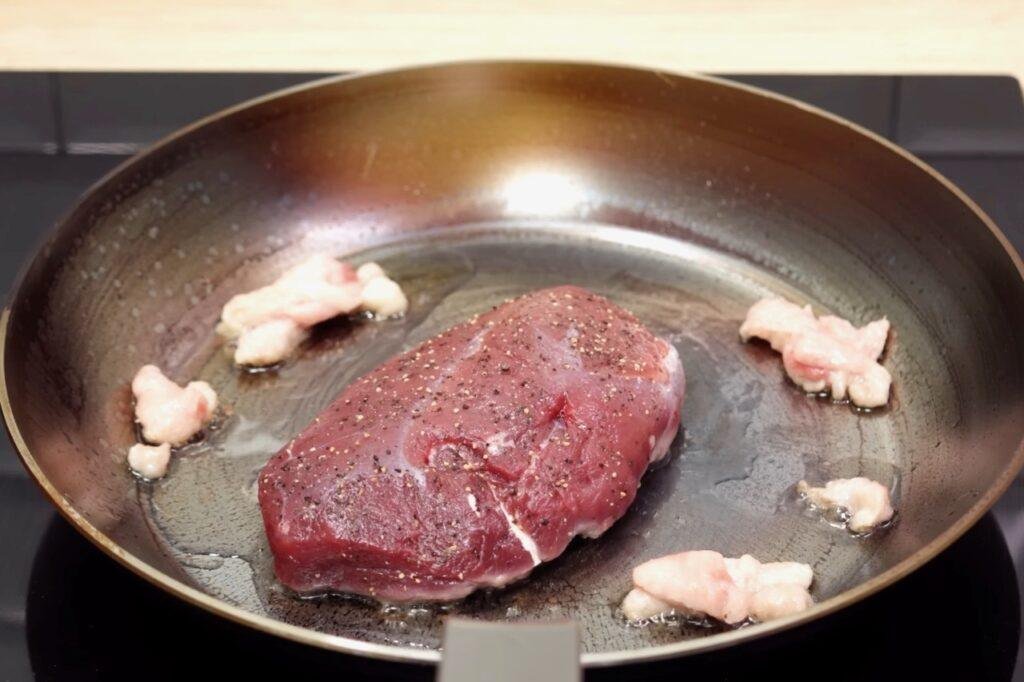 Seasoned raw duck breast in a dark frying pan with pieces of fat