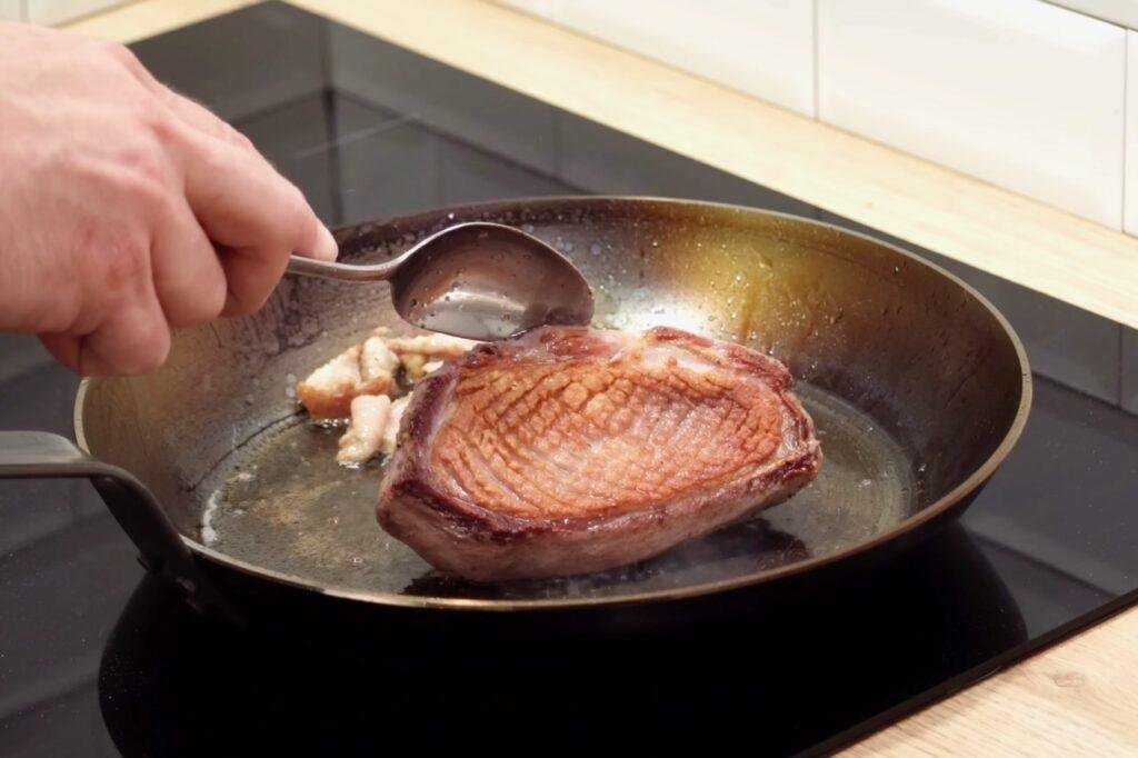 Spoon basting a golden seared duck breast in a frying pan
