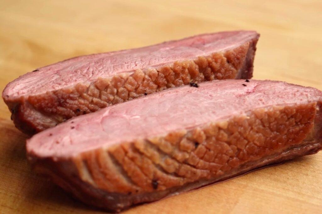 Two halves of roasted duck breast with golden skin and pink meat on a wooden board