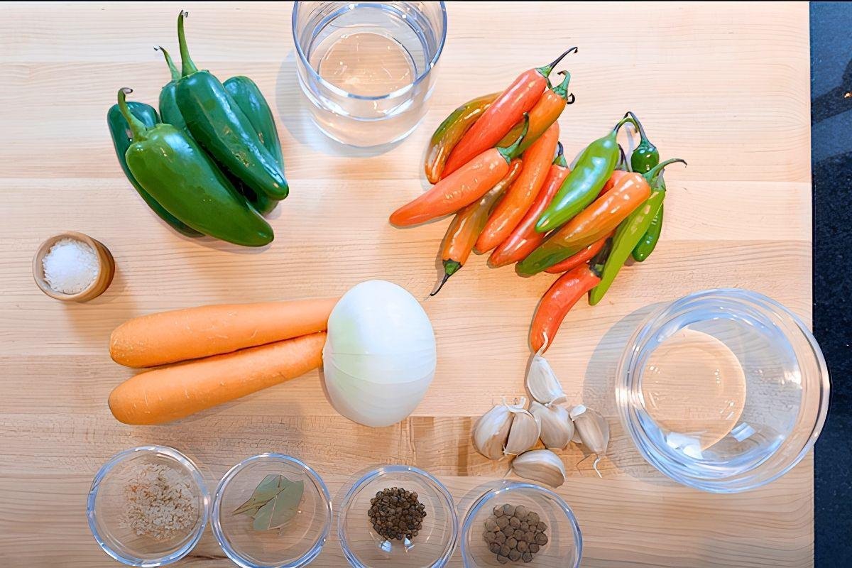 Overhead view of escabeche ingredients: green and red chillies, carrots, onion, garlic, spices and water on a wooden board