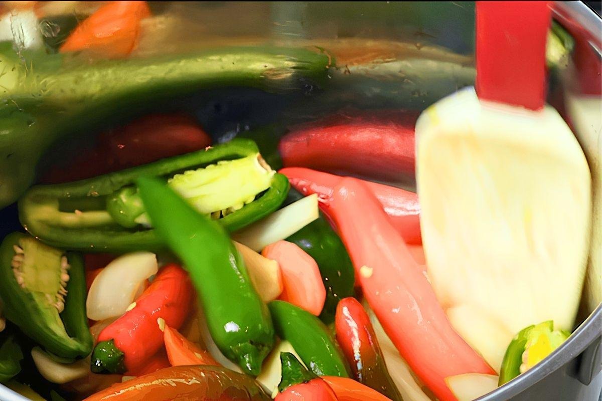 Close up of green and red chillies and onion being pickled in a steel pot