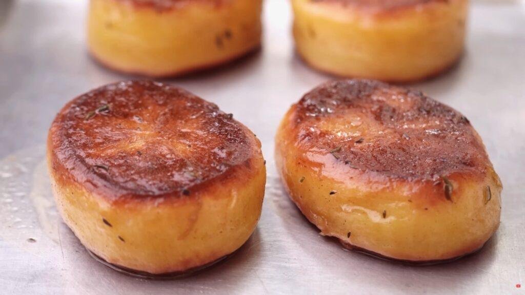 Golden brown fondant potatoes with caramelised tops on a lined baking tray