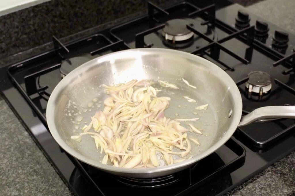 Sliced shallots softening in a steel pan on a gas hob