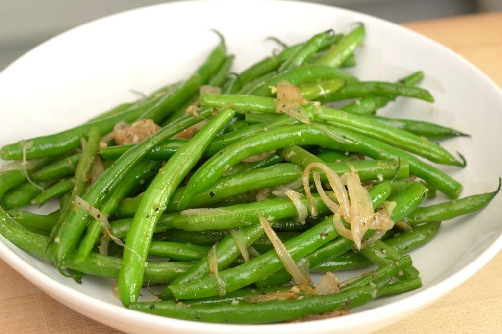 White bowl of green beans with golden fried garlic slivers
