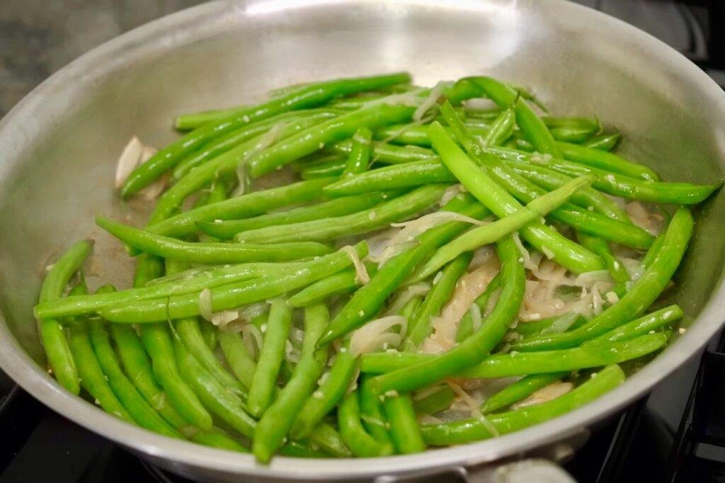 Green beans steaming in a steel pan with shallots and garlic