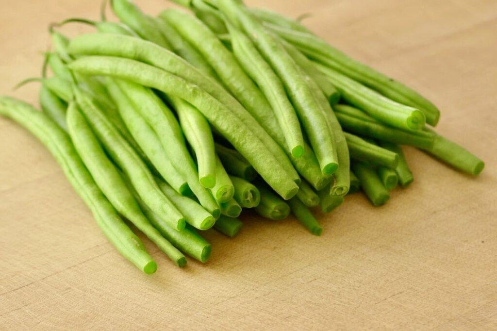 Pile of trimmed raw green beans on a wooden cutting board
