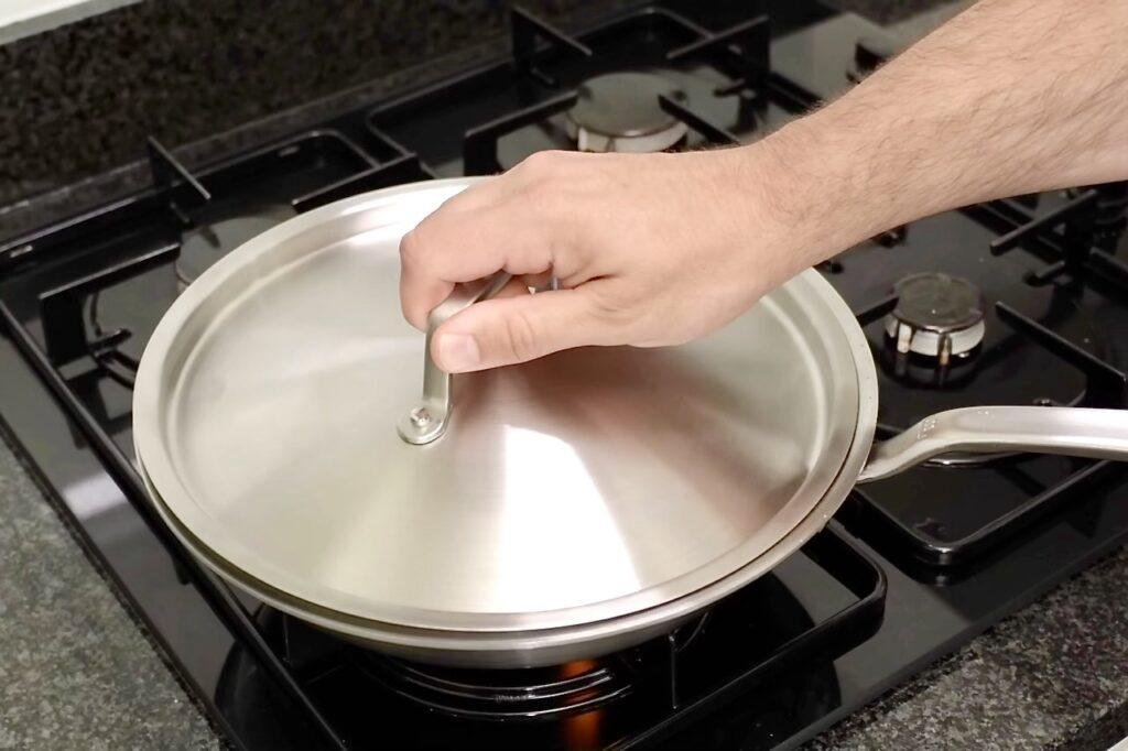 Hand placing a steel lid on a pan of green beans on the hob