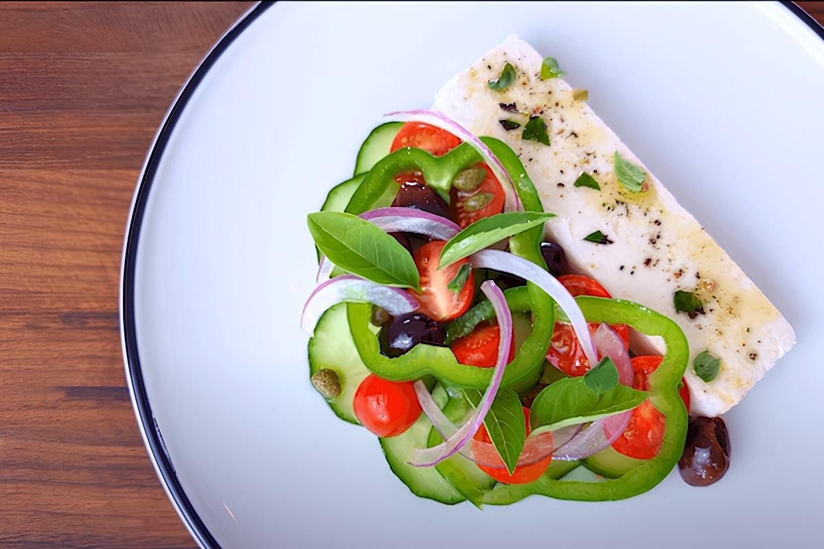 Greek salad with a slab of feta, cucumber, green pepper, tomatoes and olives on a white plate