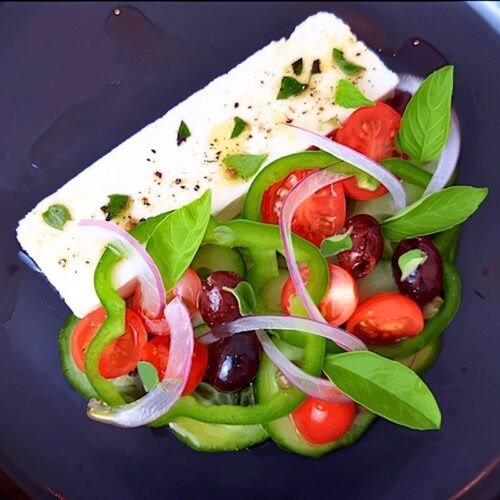 Overhead view of Greek salad with feta, green pepper, tomatoes, red onion, olives and basil on a dark plate