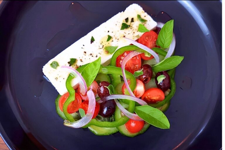 Overhead view of Greek salad with feta, green pepper, tomatoes, red onion, olives and basil on a dark plate