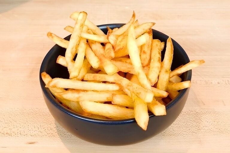 Black bowl of golden french fries on a wooden board