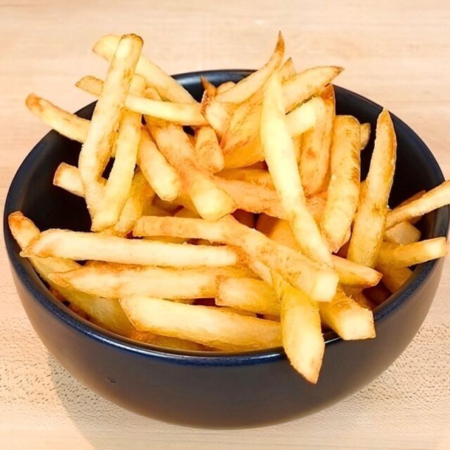 Black bowl of golden french fries on a wooden board
