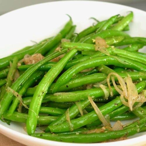 White bowl of bright green beans topped with golden fried shallot