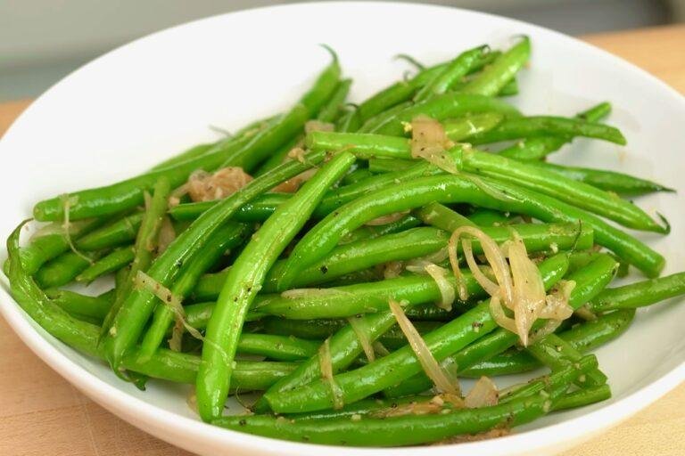 White bowl of bright green beans topped with golden fried shallot