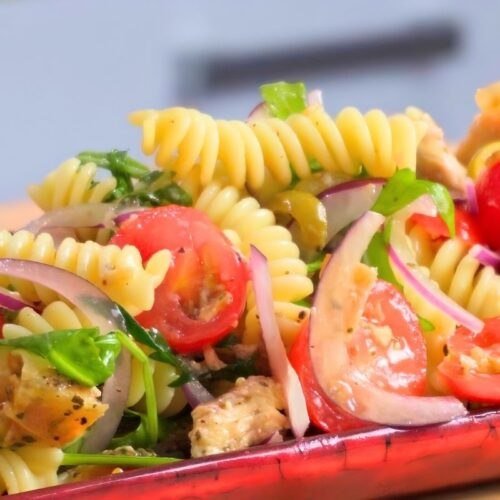 Italian chicken pasta salad with fusilli, cherry tomatoes, red onion and rocket on a red platter