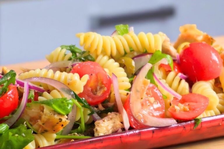 Italian chicken pasta salad with fusilli, cherry tomatoes, red onion and rocket on a red platter