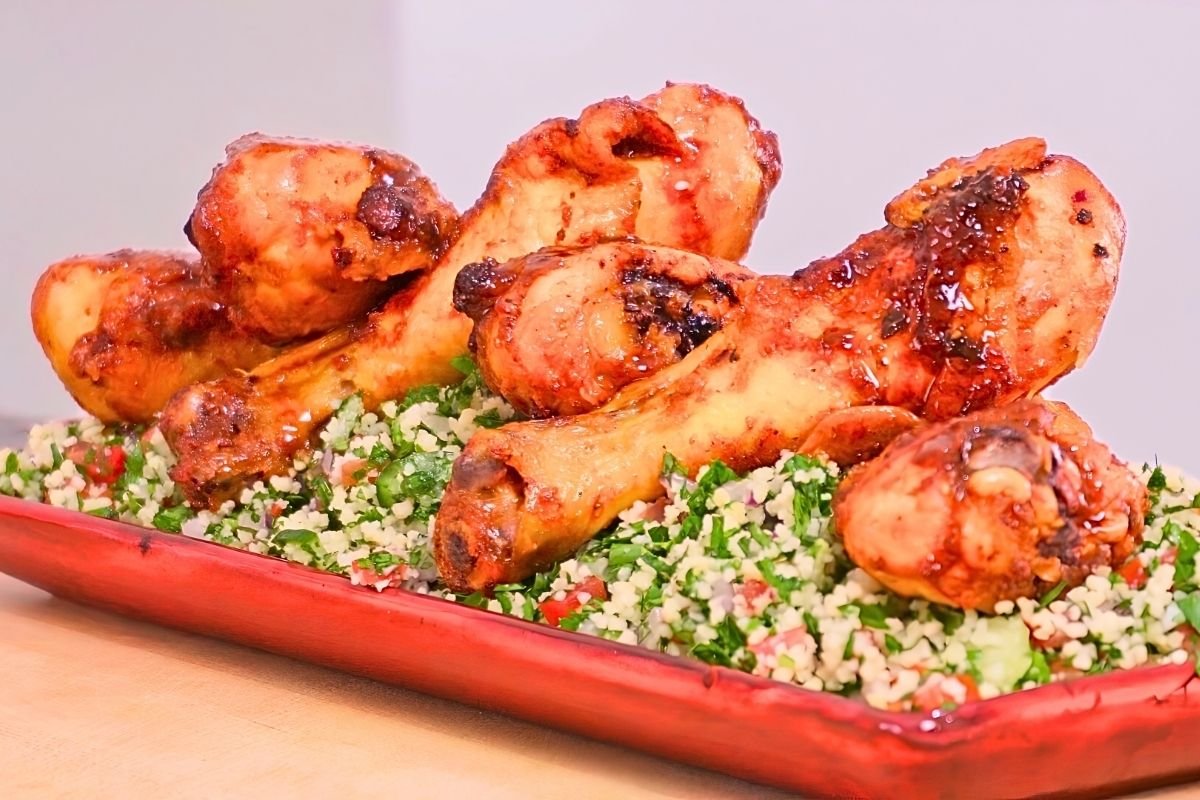 Red platter of glazed chicken drumsticks on a bed of tabbouleh salad
