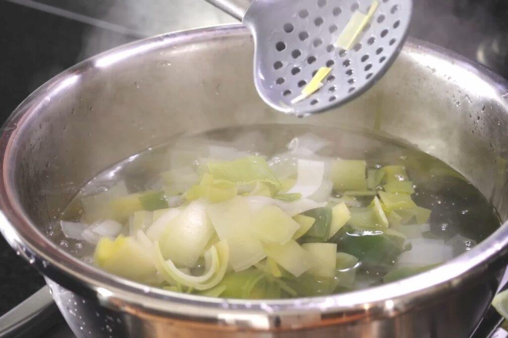 Slotted spoon lifting sliced leeks from a pot of hot water