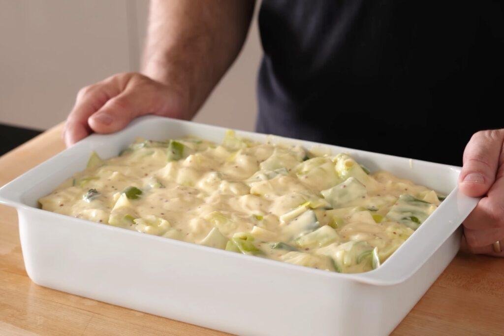 Person holding a white baking dish of chopped leeks in creamy sauce