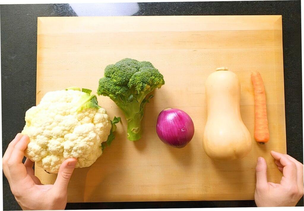 cauliflower, broccoli, red onion, butternut squash and a carrot on a chopping board