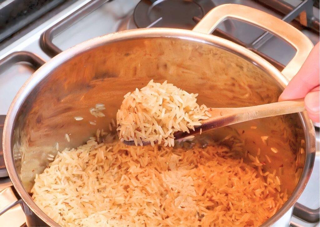Uncooked rice being toasted in a stainless steel pot and stirred with a wooden spoon