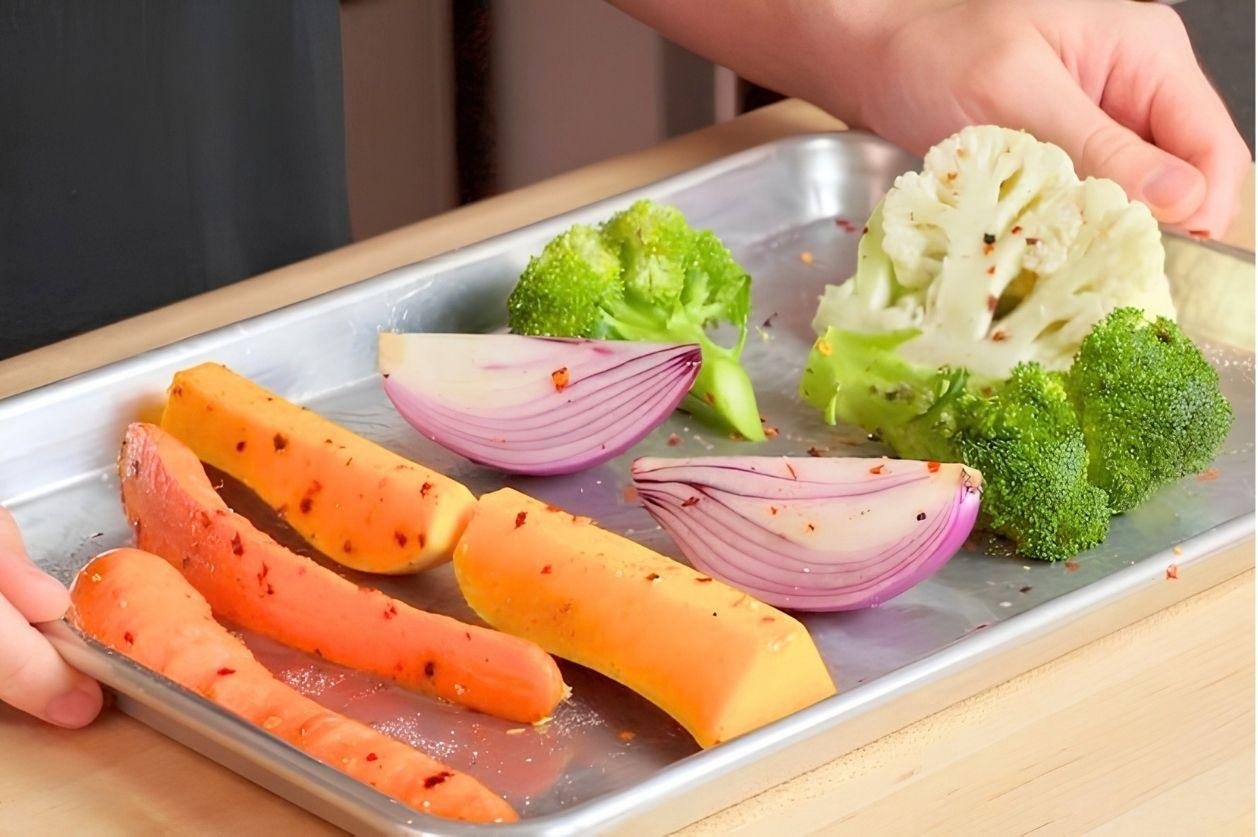 Tray of raw cauliflower, broccoli, red onion and carrot wedges with chilli flakes, ready to roast