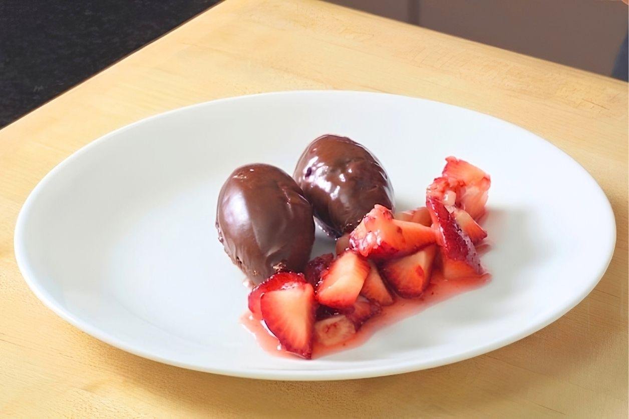 Plate of two chocolate coated mousse quenelles with macerated strawberries and juice