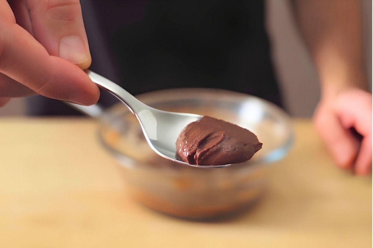 Spoon lifting smooth chocolate mousse mixture over a glass bowl