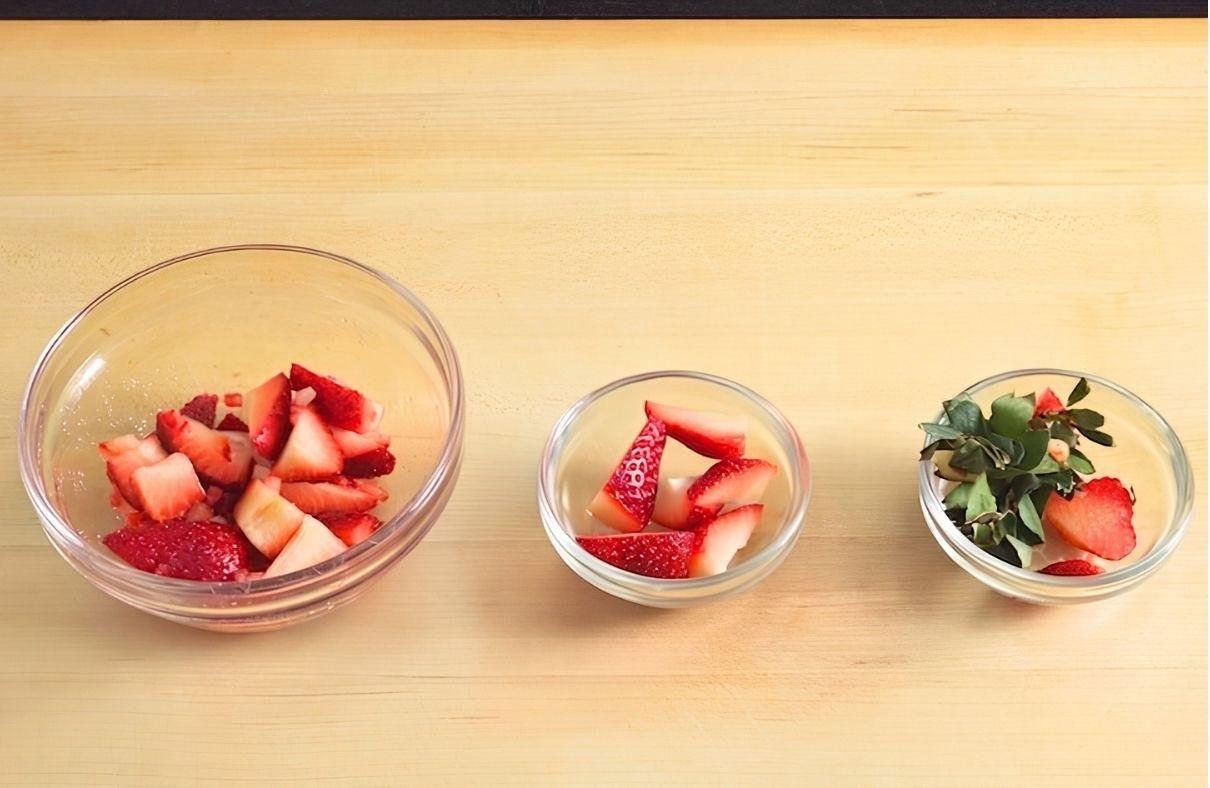 Three glass bowls of diced strawberries in different amounts on a wooden counter