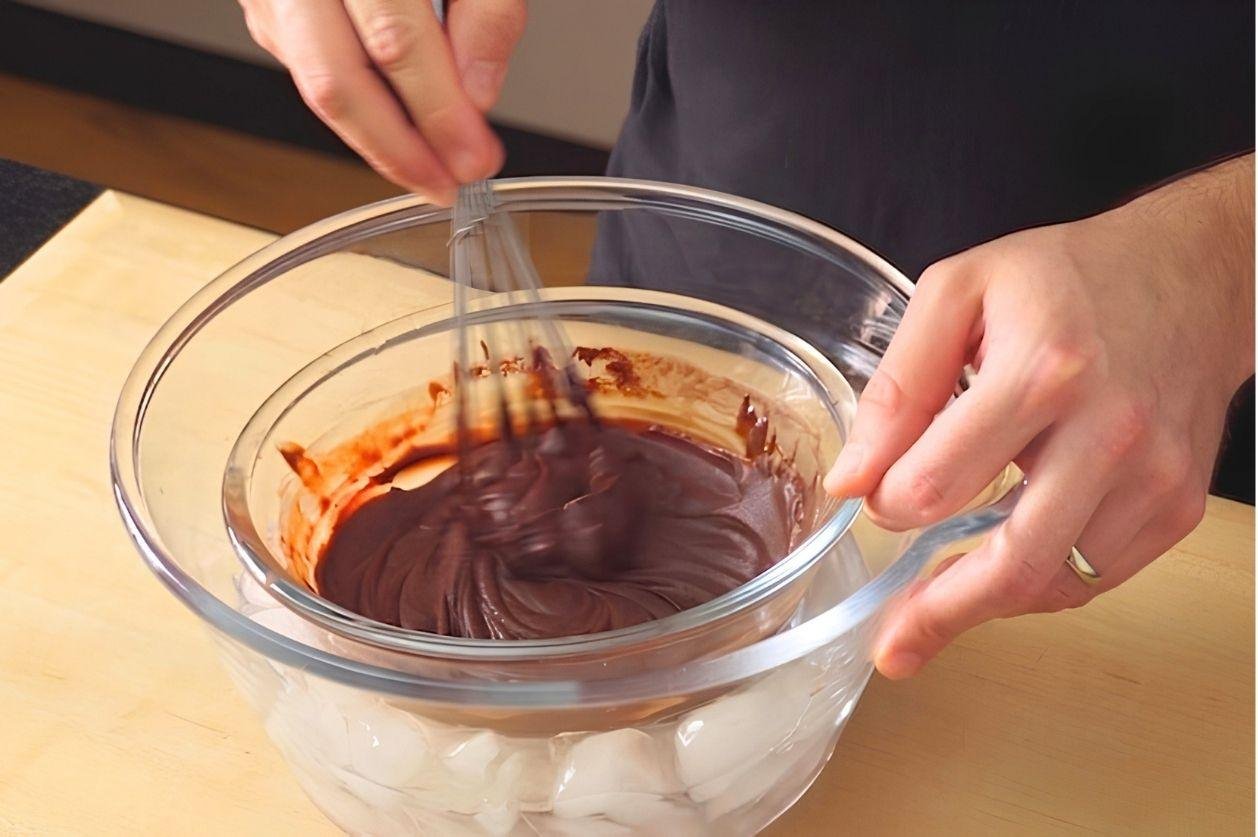 Hand whisking melted chocolate in a glass bowl set over a bowl of ice
