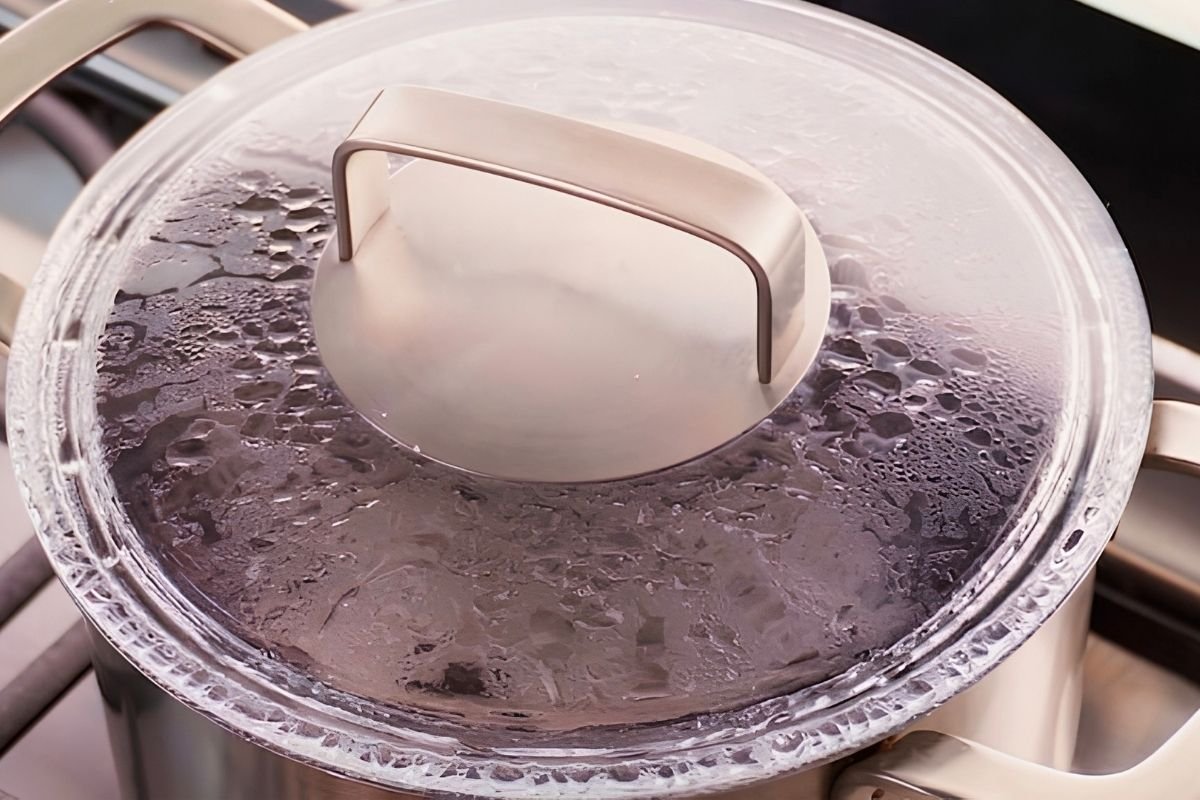 Steel pot covered with a glass lid on the hob while black beans and rice steam
