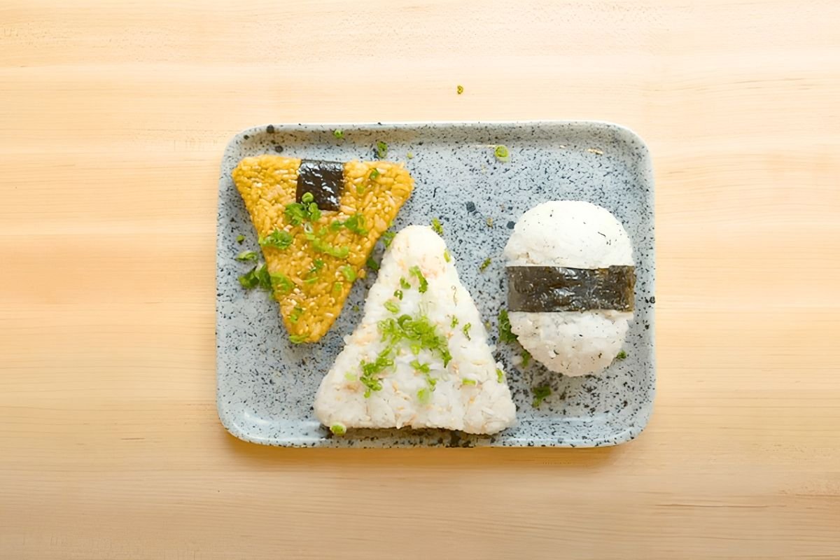 Three onigiri on a small blue tray seen from above on a wooden board
