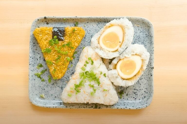 Overhead view of three onigiri on a speckled blue tray: soy glazed, plain with spring onion, and a soy egg wrapped in rice