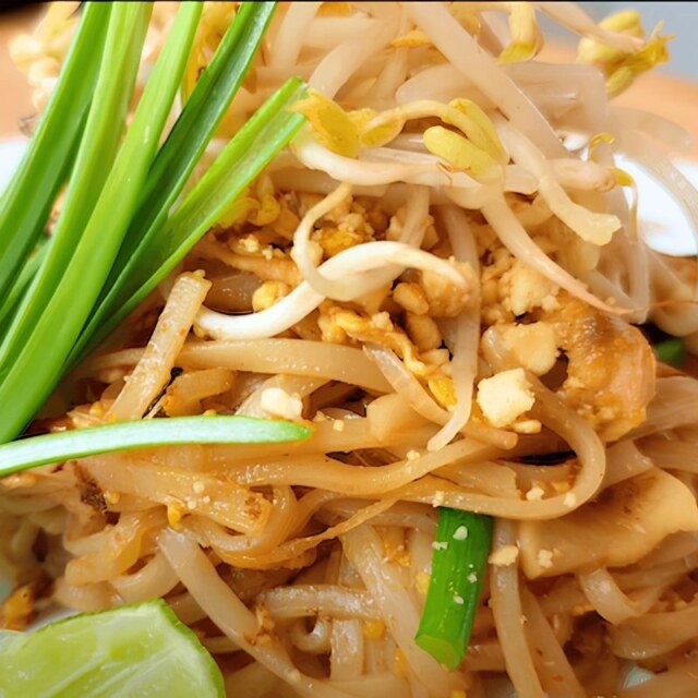 Close up of pad thai noodles topped with bean sprouts, garlic chives and a lime wedge