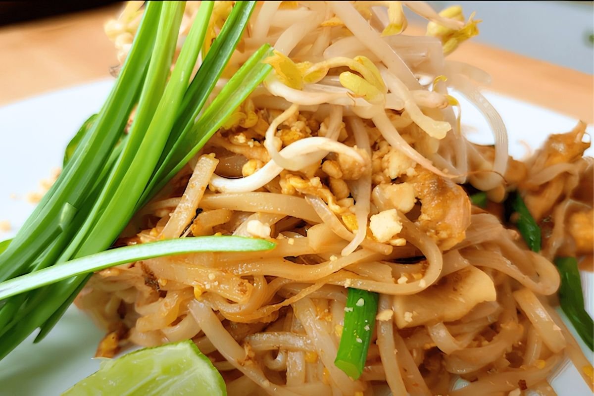 Close up of pad thai noodles topped with bean sprouts, garlic chives and a lime wedge