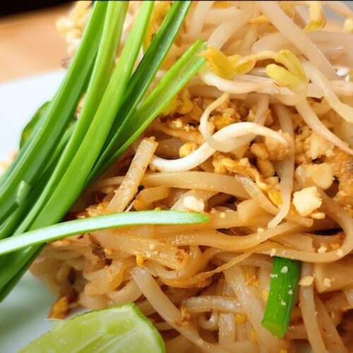 Close up of pad thai noodles topped with bean sprouts, garlic chives and a lime wedge