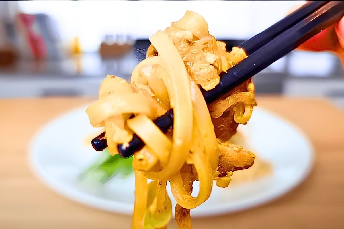 Chopsticks lifting a twirl of pad thai noodles with chicken