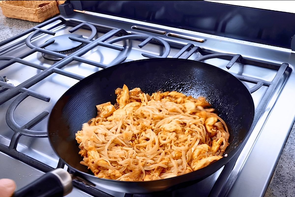 Chicken pad thai being stir fried in a black wok on the hob